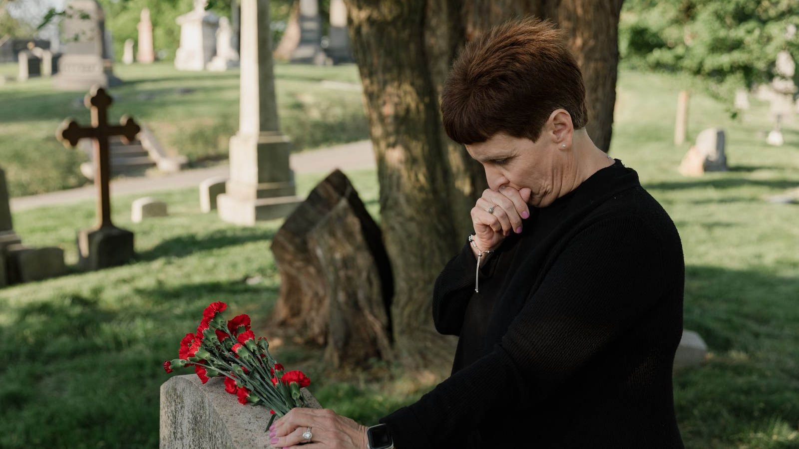 Mulher vestida de preto deposita flores vermelhas sobre uma lapide em um cemiterio, representando o falecimento que da origem a pensao por morte