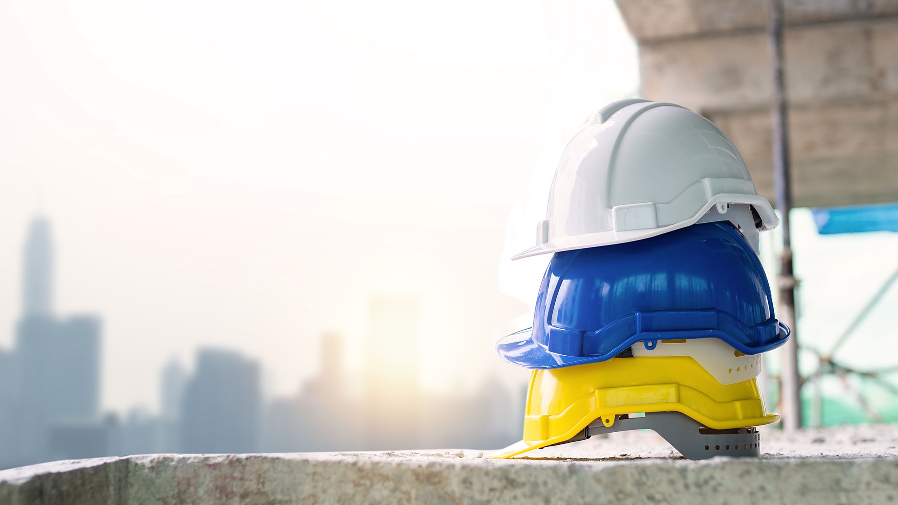 Tres capacetes de seguranca empilhados sobre uma laje de concreto em obra, equipamento de protecao individual que a NR-6 obriga o empregador a fornecer gratuitamente
