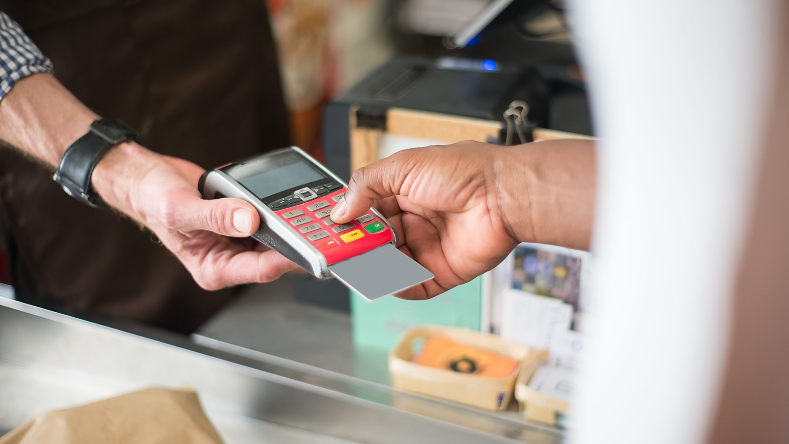 Cliente digita a senha do cartao na maquineta segurada pelo vendedor no balcao, pagamento parcelado em que os juros do financiamento integram o valor da venda