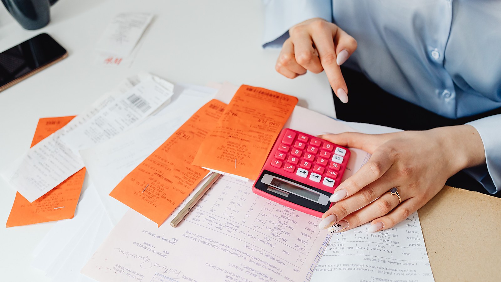 Mulher confere notas fiscais e cupons com uma calculadora sobre a mesa, conferencia da base de calculo da comissao sobre o valor total da venda a prazo