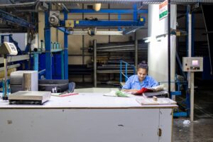 Trabalhadora de fábrica têxtil confere documentos em mesa de inspeção industrial