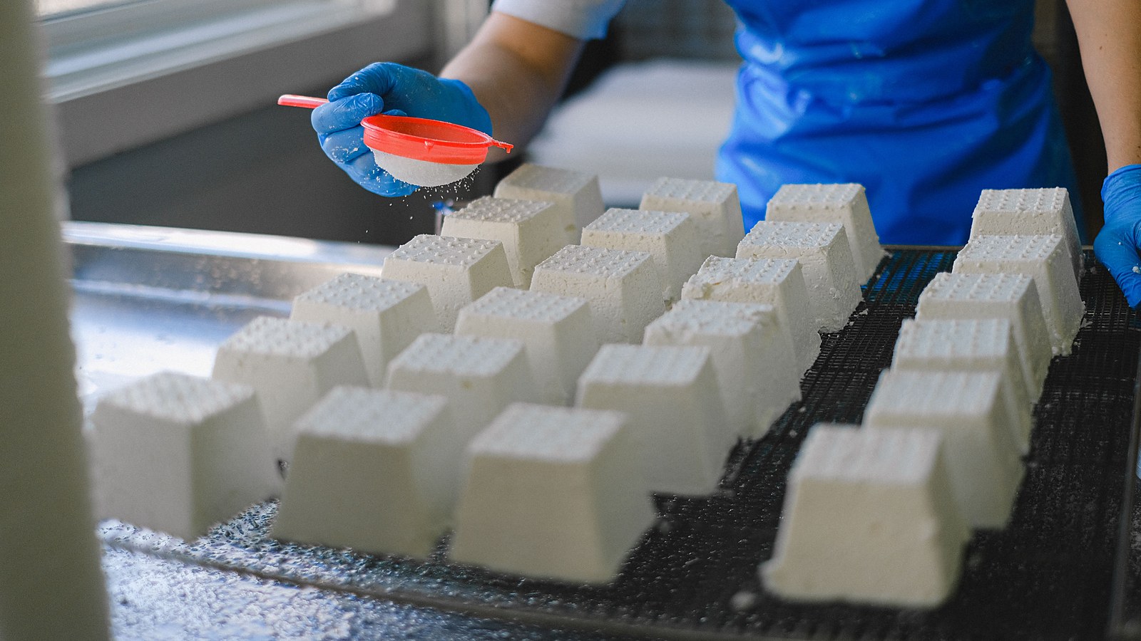Trabalhador de avental e luvas manipula alimentos na linha de producao de uma industria