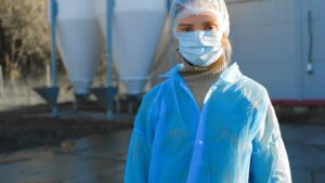 Trabalhadora de frigorifico paramentada com touca descartavel, mascara e avental na area industrial