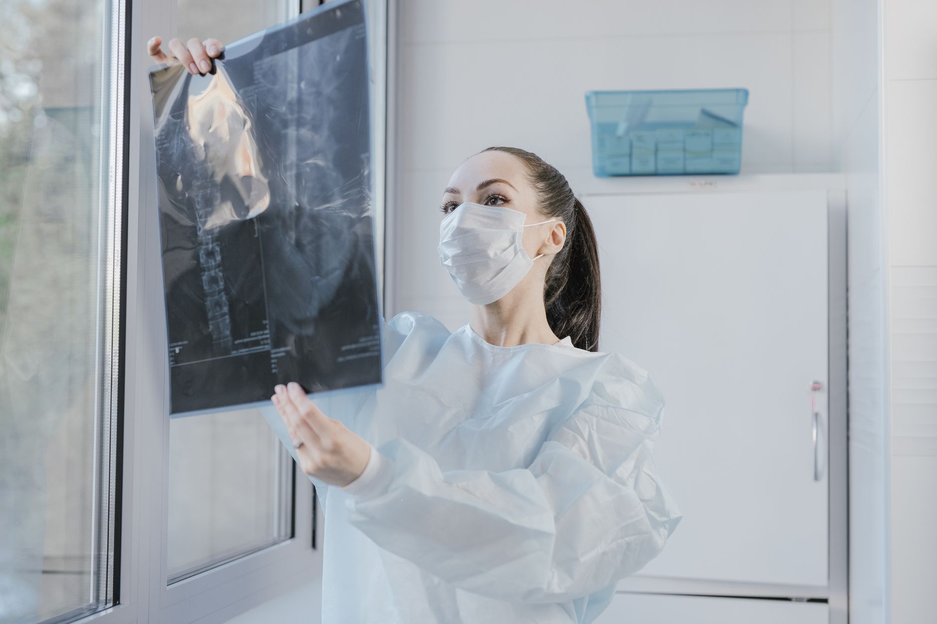 Laudo médico e radiografia de ombro sobre uma bancada de aço inox de frigorífico, ao lado de uma faca de desossa e de uma munhequeira ortopédica, símbolo da disputa entre doença degenerativa e doença ocupacional