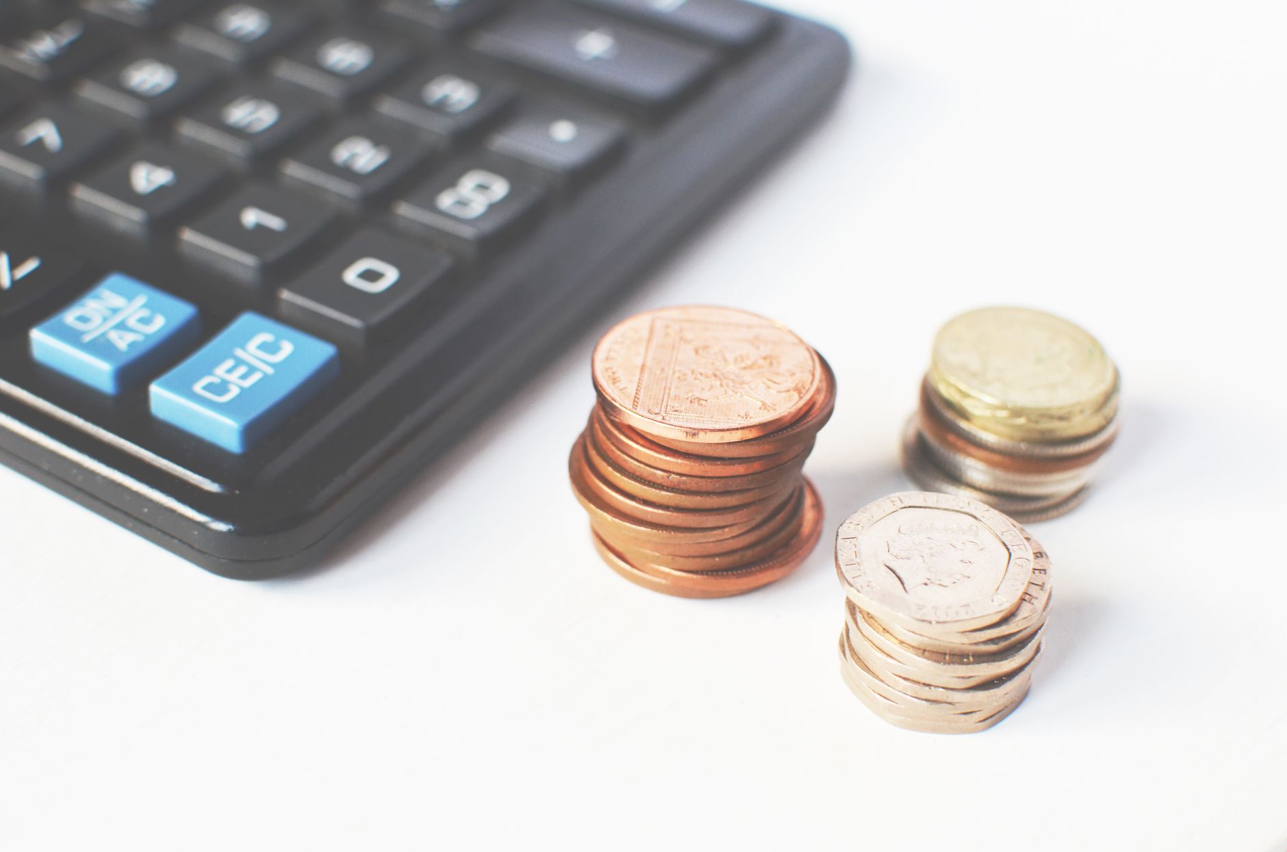 Contracheque, calculadora e moedas empilhadas sobre a mesa ao lado de um calendário com um domingo e um feriado destacados, representando o pagamento em dobro do domingo ou feriado trabalhado sem folga compensatória