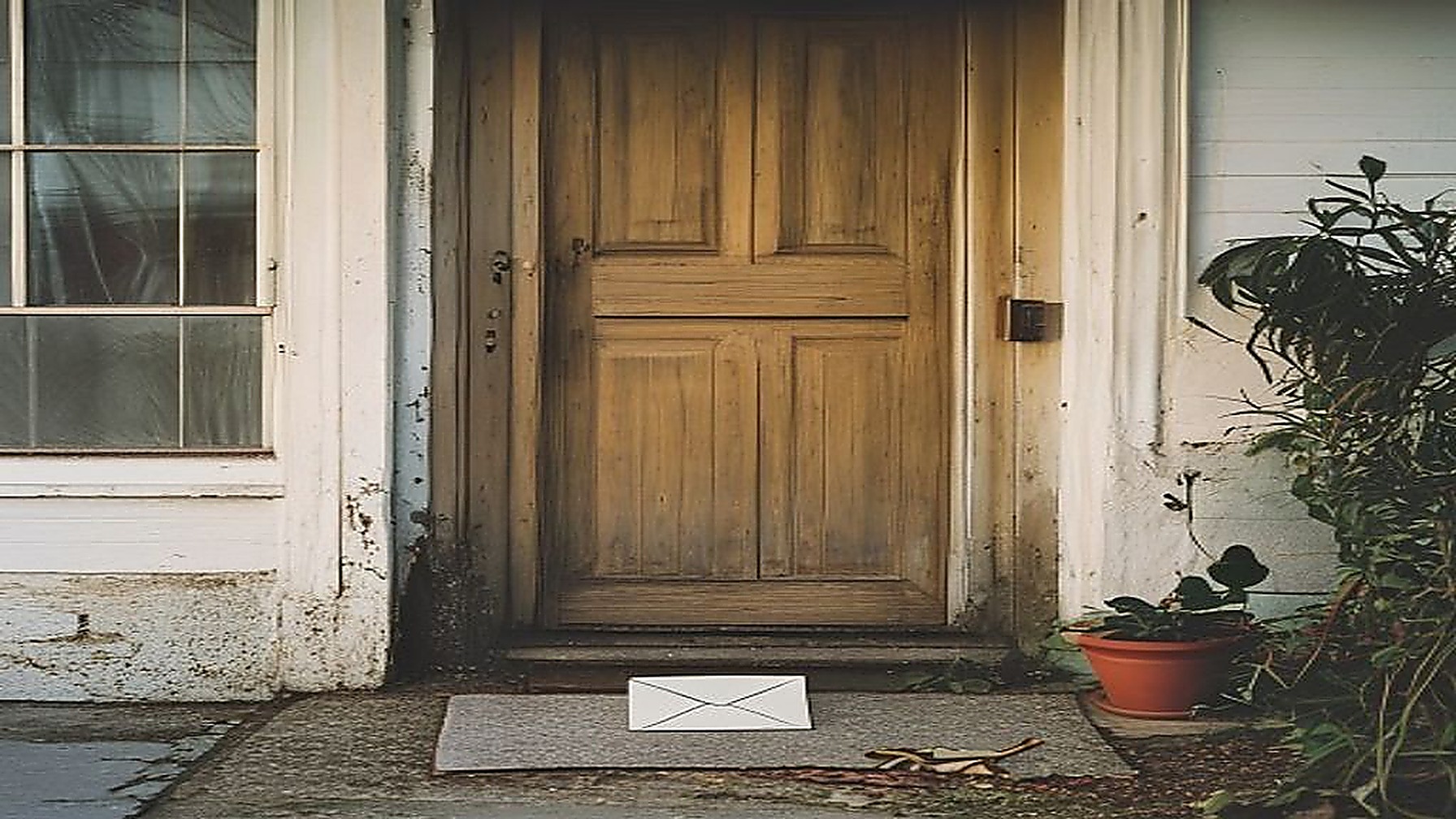 Porta de entrada de uma casa simples vista da rua, com um envelope de correspondência oficial pousado sobre o capacho, representando a visita domiciliar do Cadastro Único exigida para o BPC de quem mora sozinho e a notificação de atualização cadastral