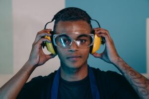 Trabalhador ajustando protetor auricular tipo concha e óculos de proteção, simbolizando a exposição ao ruído no frigorífico