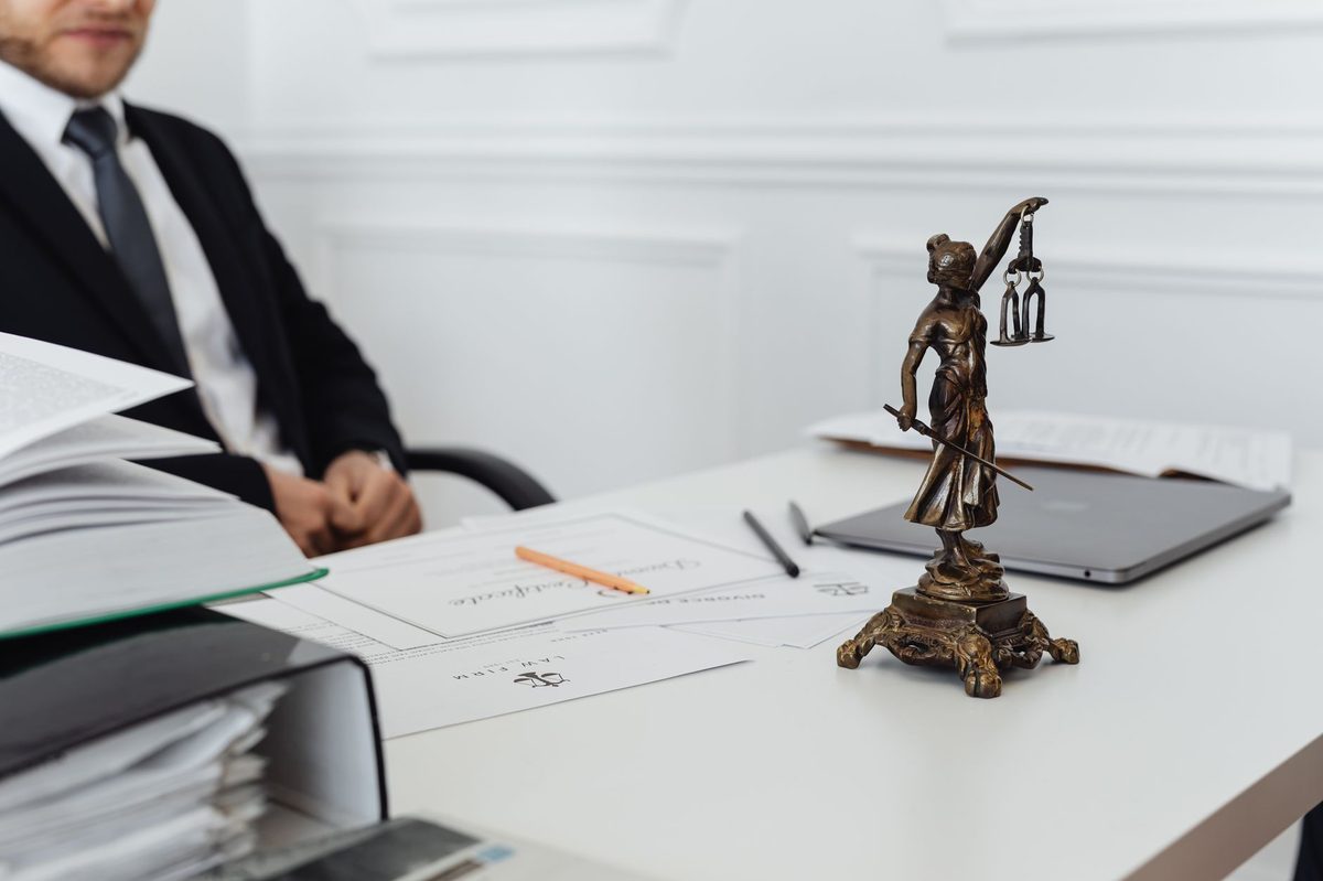 Advogado a mesa com documentos juridicos e a estatua da Justica