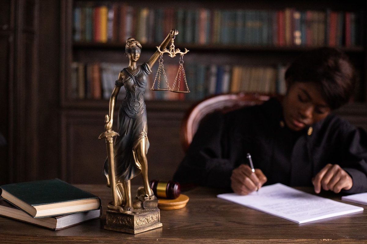 Estatua da Justica, martelo e livros de direito sobre a mesa de um tribunal